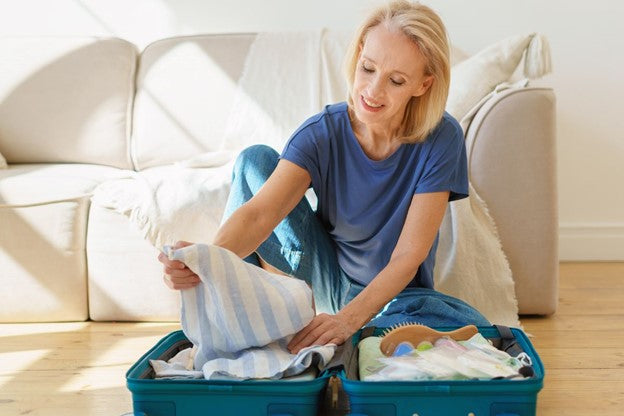 a old woman wearing blue dress organizing her luggae with clothes