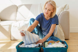 a old woman wearing blue dress organizing her luggae with clothes