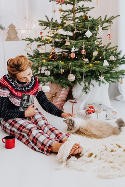 Woman enjoying a cozy Christmas with her cat beside a decorated tree and gifts.