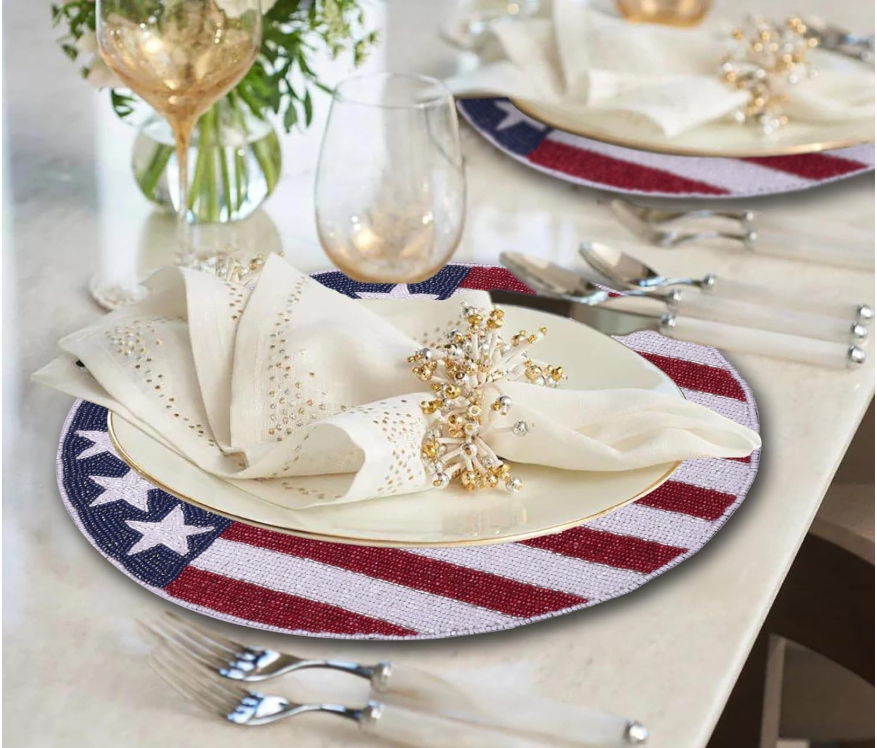Elegant dining table setup featuring USA flag-themed placemats with red, white, and blue beaded stars and stripes, paired with ivory napkins and gold napkin rings.
