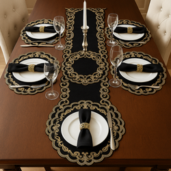 Elegant dining table setup featuring a black and gold embroidered table runner with matching round placemats, fine white dinnerware, and gold napkin rings.