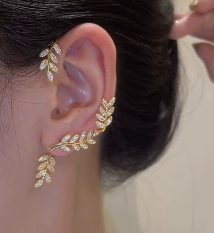 Gold female stud earrings with leaf design, hanging from the left ear in a close-up image of Lamp Post women earrings.